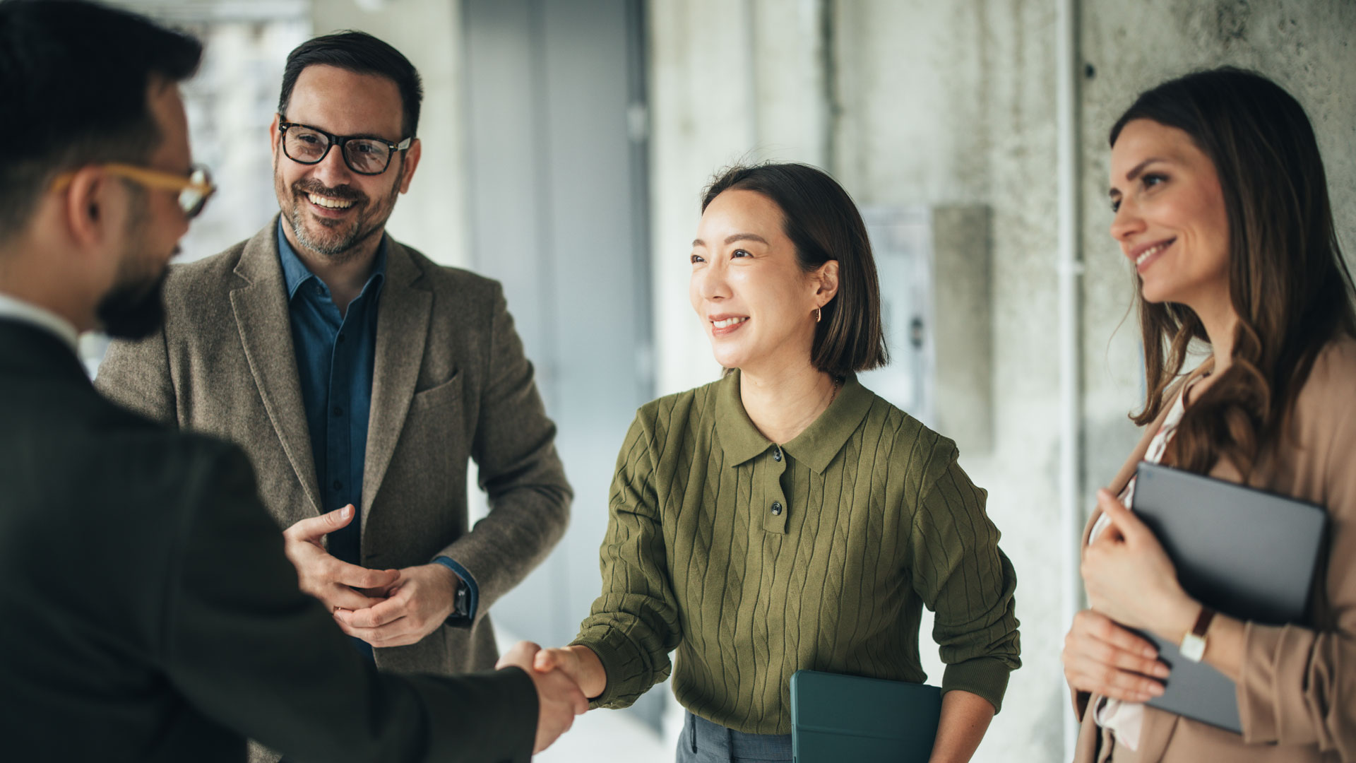 Business professionals greeting and welcoming a colleague with a handshake in a modern office environment. Team members holding coffee and engaging in friendly conversation, representing professional networking, teamwork, partnership, and positive workplace relationships, ekas, fieldwork partners