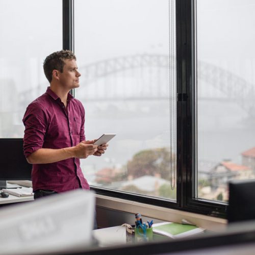 Businessman using tablet computer in office, he's looking through the window with the Sydney harbour bridge in the background.